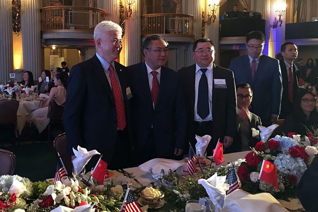 Three gentlemen in suits are pictured smiling behind a formal dinner table
