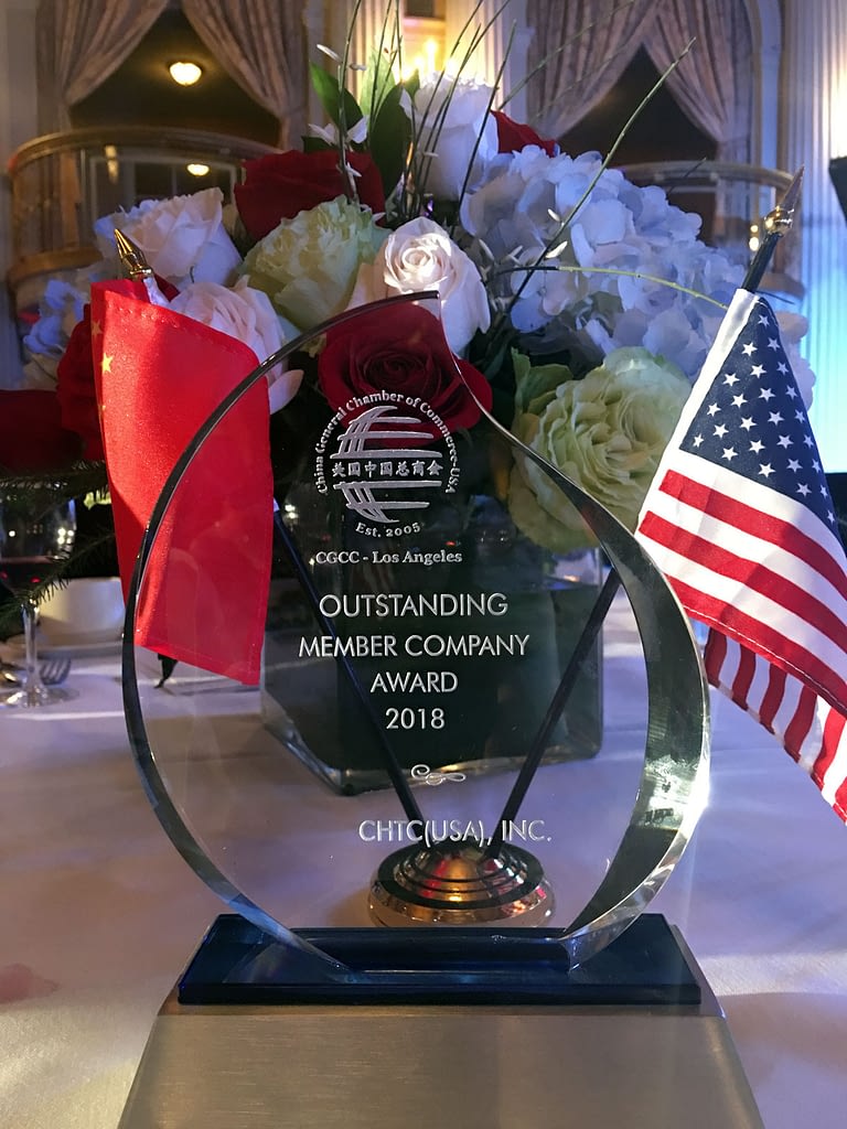 An award on a table in front of a floral centerpiece with American and Chinese flags